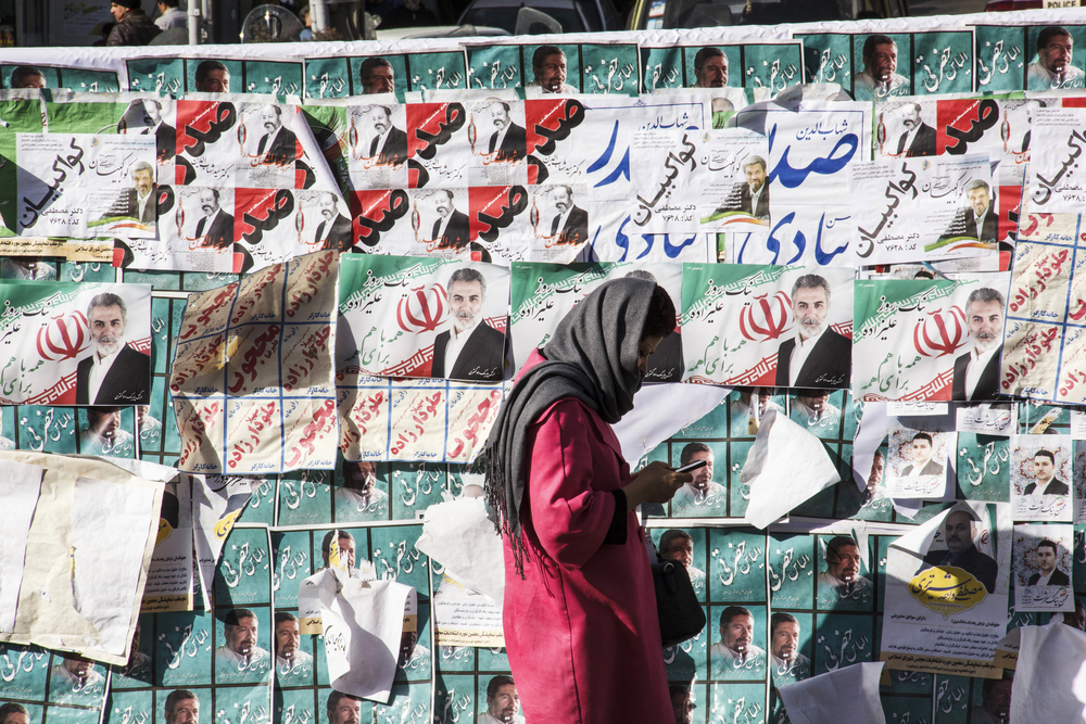 A young woman walks by election posters in Iran.