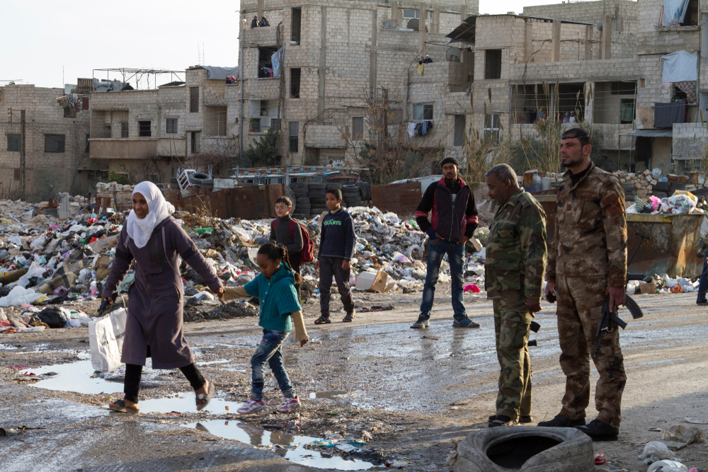 Syrian civilians walk past armed soldiers in war-torn Douma, Syria, 2015. (Shutterstock)