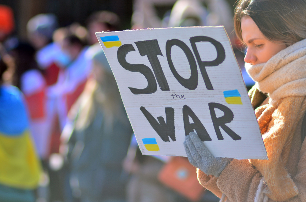 A woman holds a sign reading "stop the war" emblazoned with Ukrainian flags.