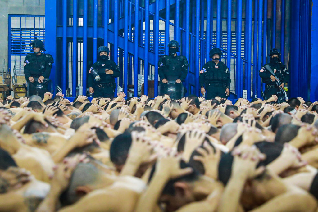 Police inspect inmates in a prison outside San Salvador, June 2023. The inmates sit shirtless and hunched over with their hands folded behind bowed heads. (Getty)