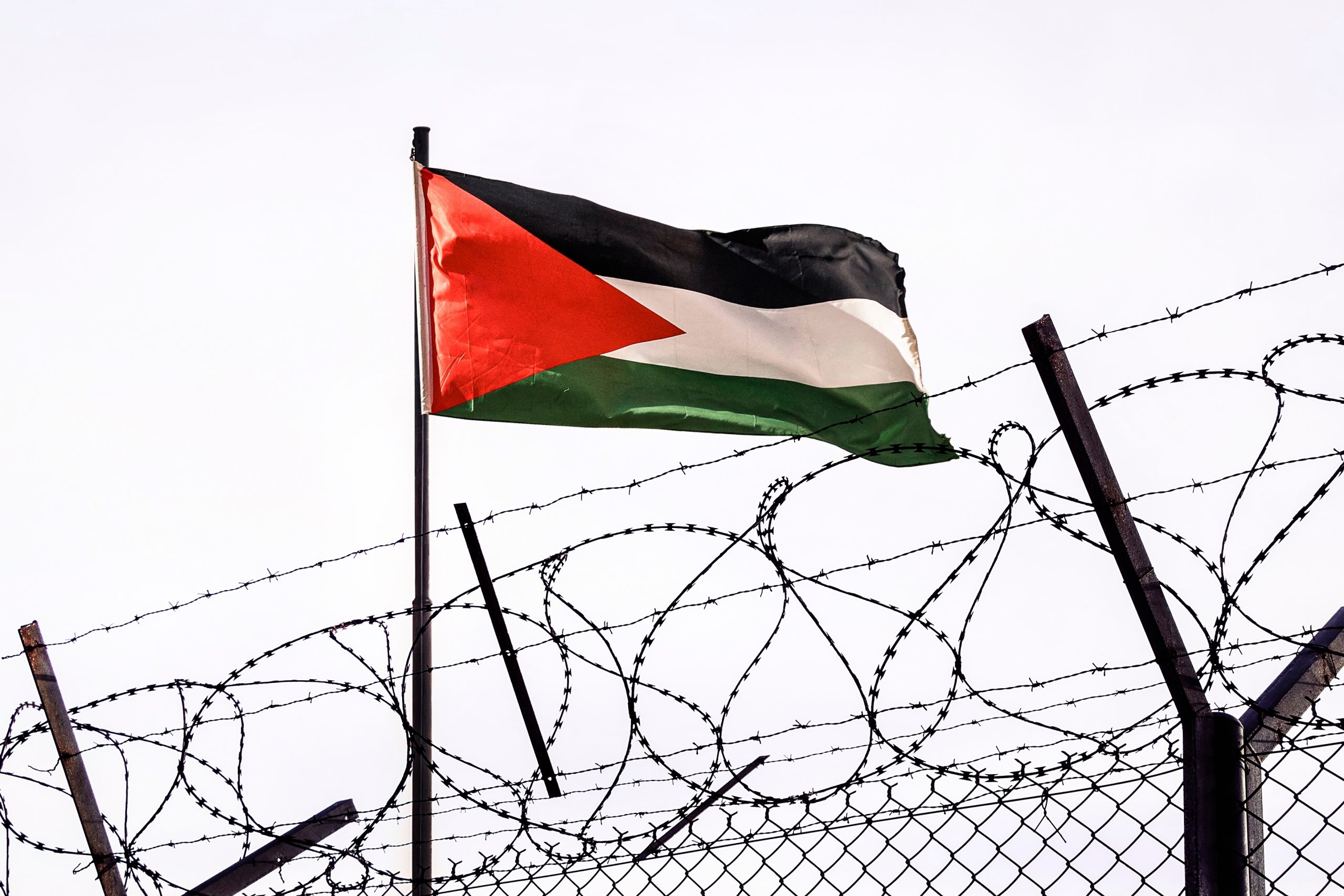 A Palestinian flag flies behind barbed war.